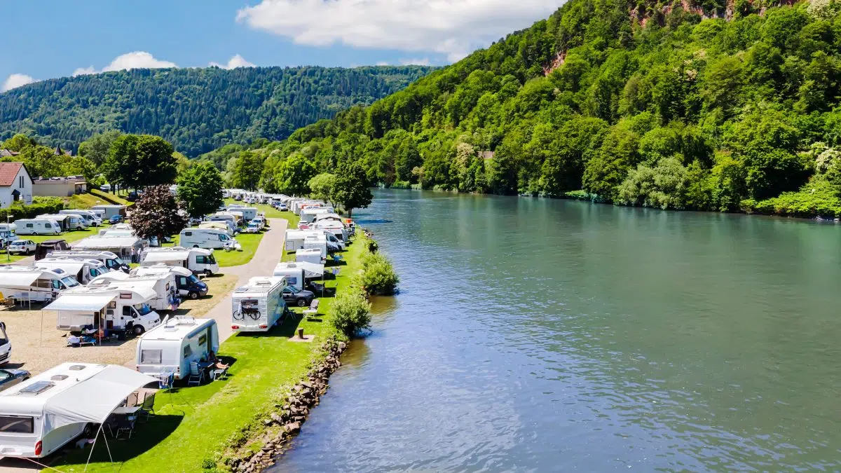 Campingplatz mit zahlreichen Wohnmobilen und Wohnwagen an einem Fluss gelegen.