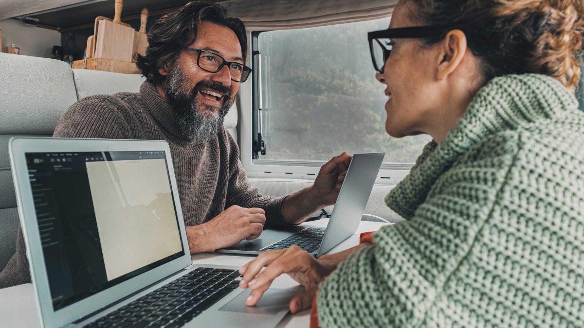 Ein Mann und eine Frau sitzen in einem Wohnmobil jeweils vor einem Laptop.